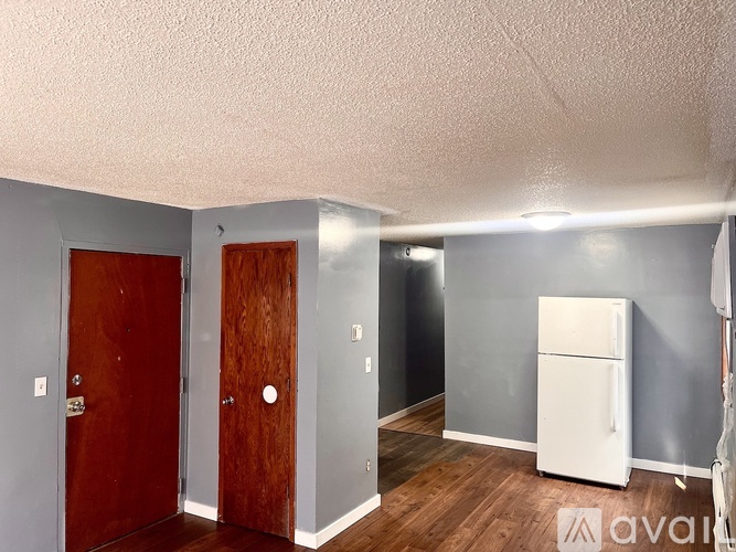 A room with a white fridge and two wooden doors.
