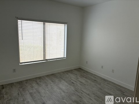 A room with a window covered by white blinds and wooden flooring.