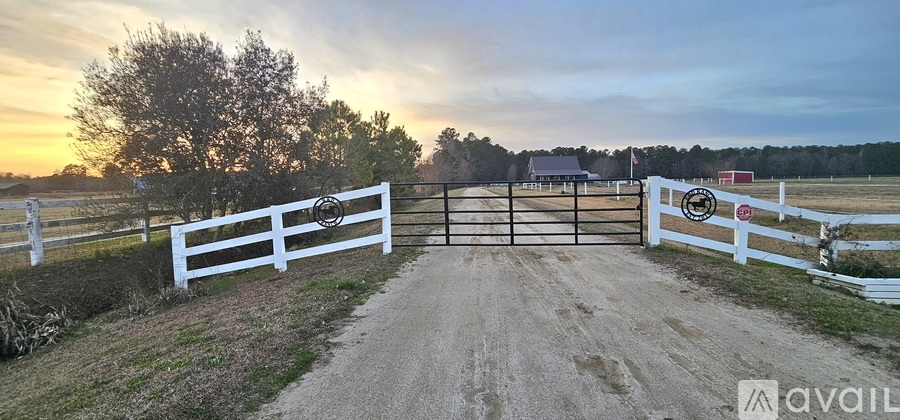 A white fence with a gate stands at the entrance to a dirt road.
