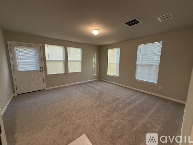 A room with beige carpet and three windows.