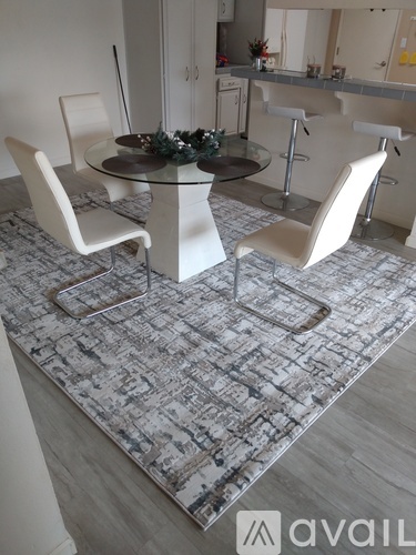A dining room with a glass table surrounded by white chairs.