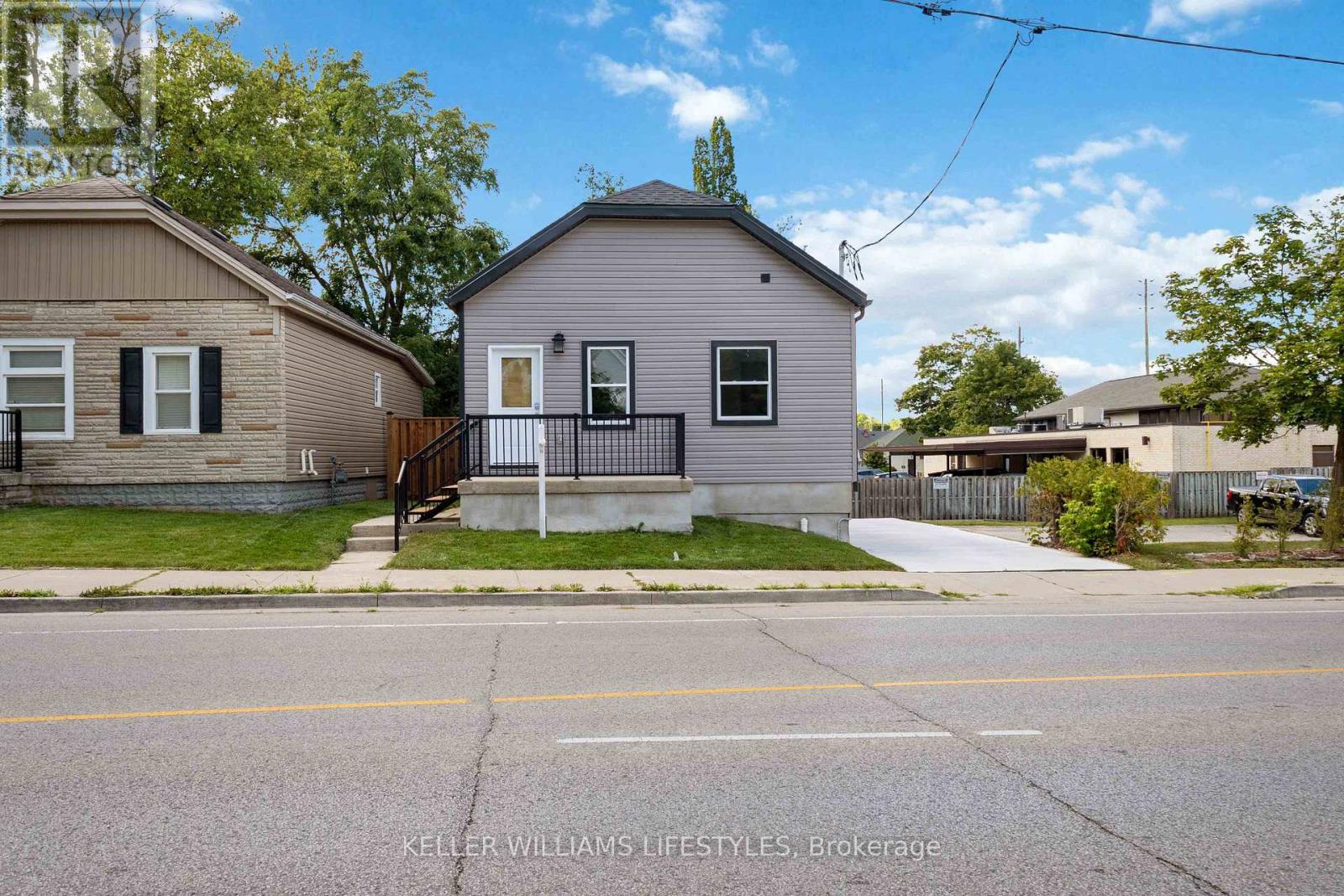 A house with a grey roof and a white door is situated on a street.