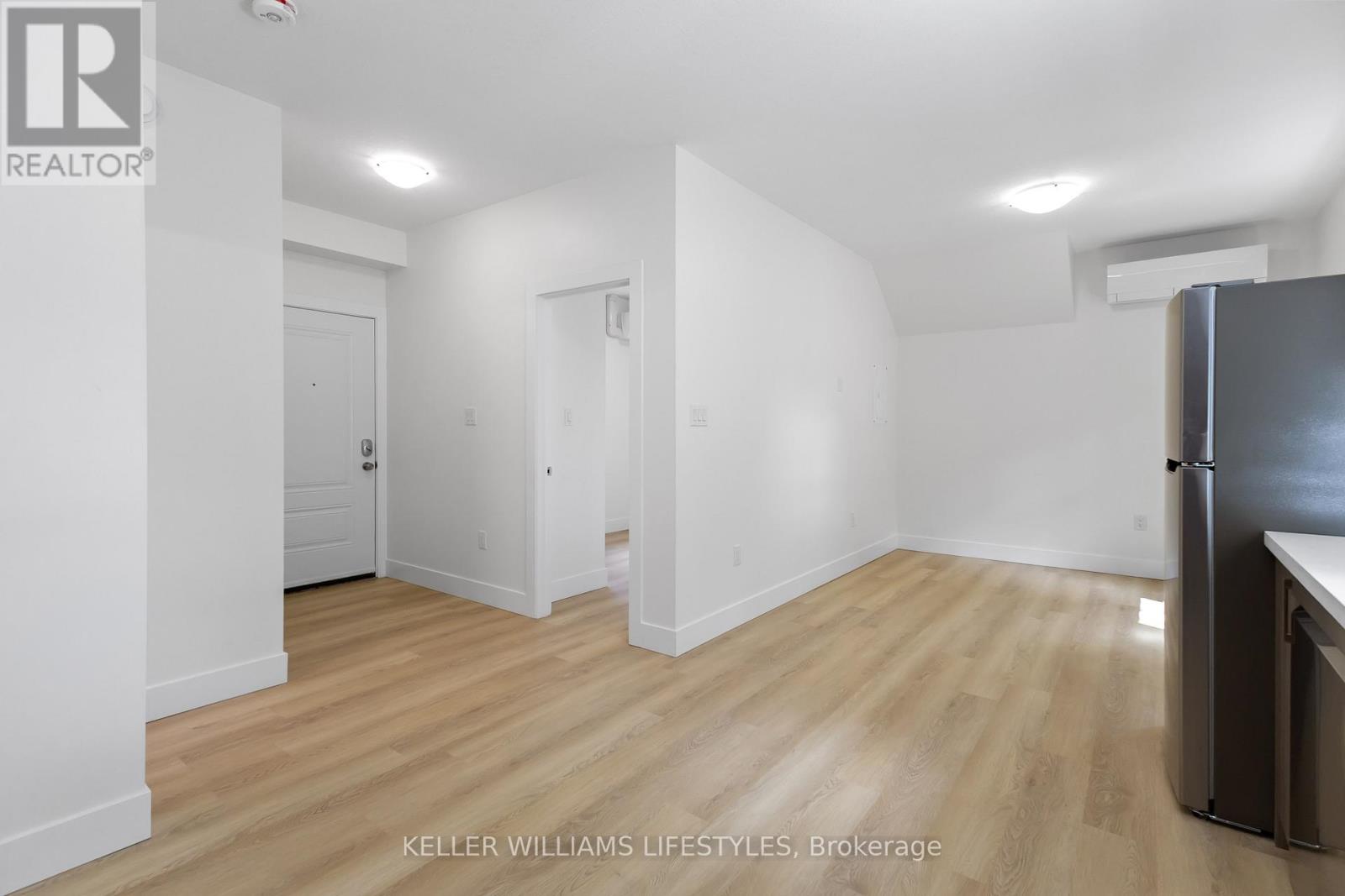 A kitchen area with a refrigerator and wooden flooring.