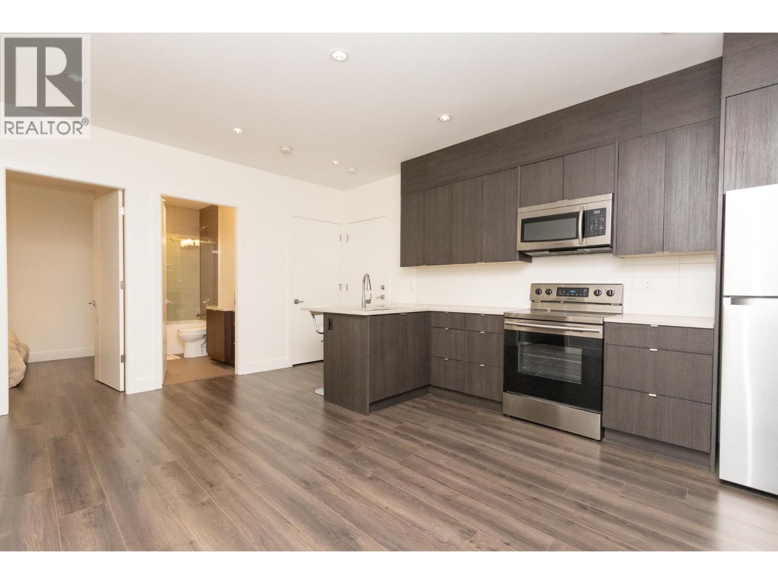 A modern kitchen with dark wood floors and stainless steel appliances.