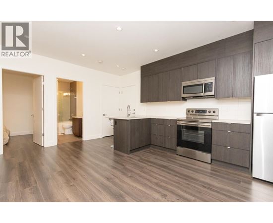 A modern kitchen with dark wood floors and stainless steel appliances.