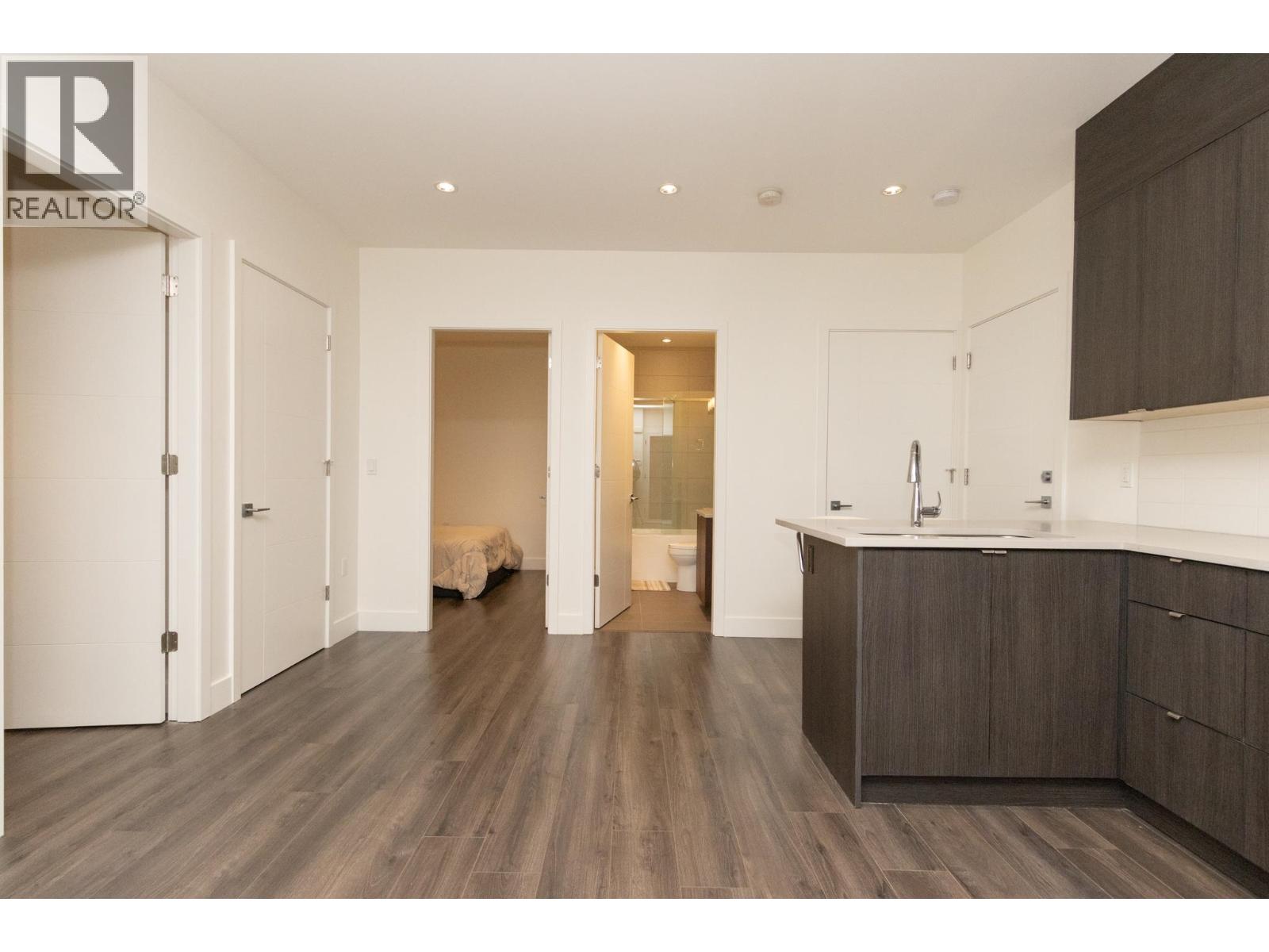 A modern kitchen with dark wood floors and white walls.