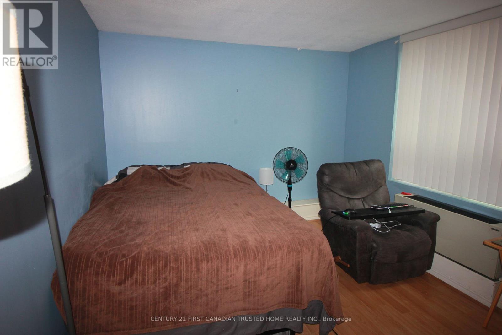 A bedroom with a bed, chair, and fan.