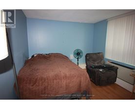 A bedroom with a bed, chair, and fan.