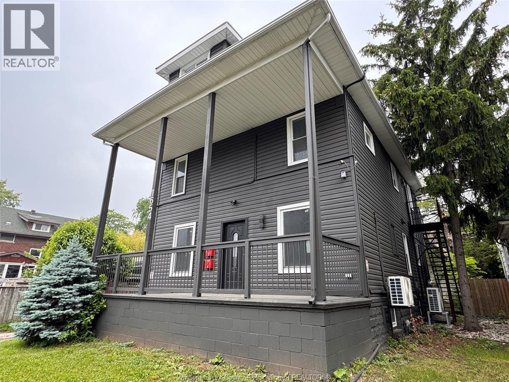 A grey house with a balcony and a tree in front.