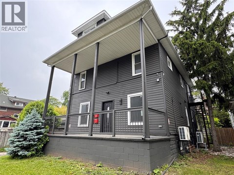 A grey house with a balcony and a tree in front.