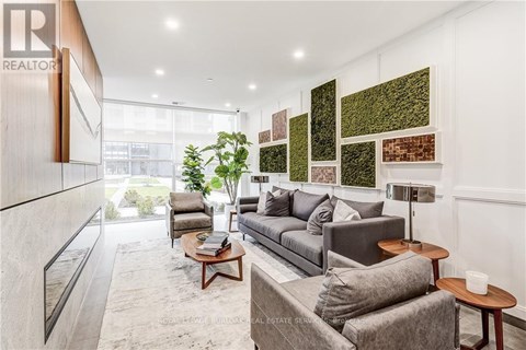 A living room with a grey couch and a green wall hanging.