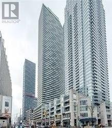 A tall building with a curved glass facade stands in front of a smaller building.