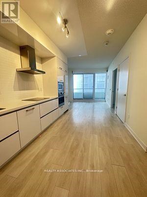 A long, narrow kitchen with white cabinets and a wooden floor.