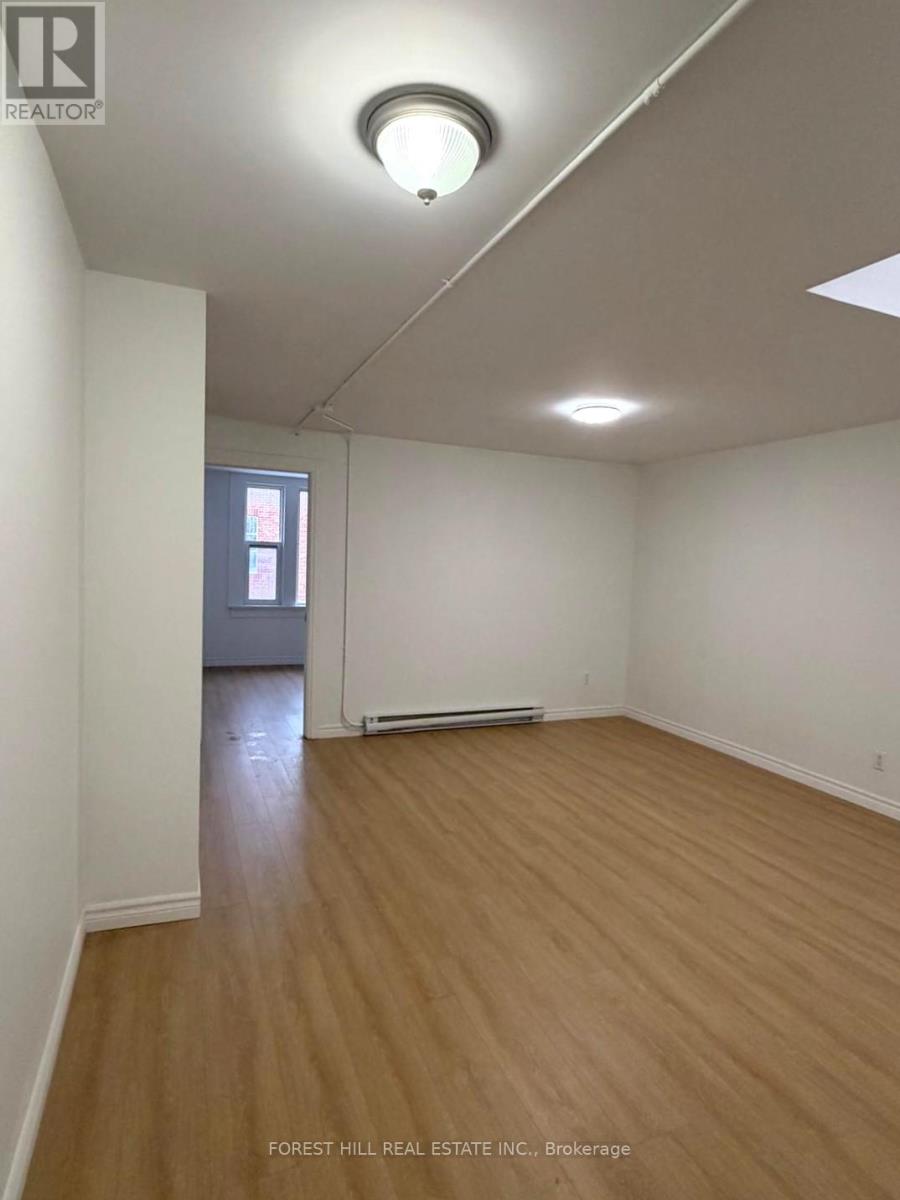 A room with wooden flooring and white walls, with a window and a door visible in the background.