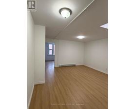 A room with wooden flooring and white walls, with a window and a door visible in the background.