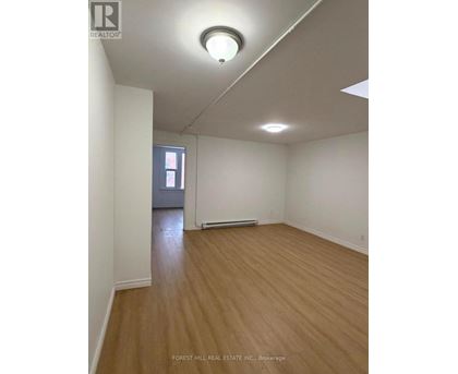 A room with wooden flooring and white walls, with a window and a door visible in the background.