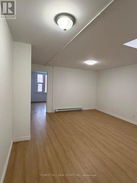 A room with wooden flooring and white walls, with a window and a door visible in the background.