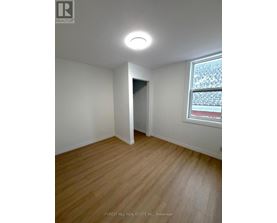 A room with a wooden floor and a window showing a red building outside.
