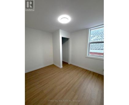 A room with a wooden floor and a window showing a red building outside.