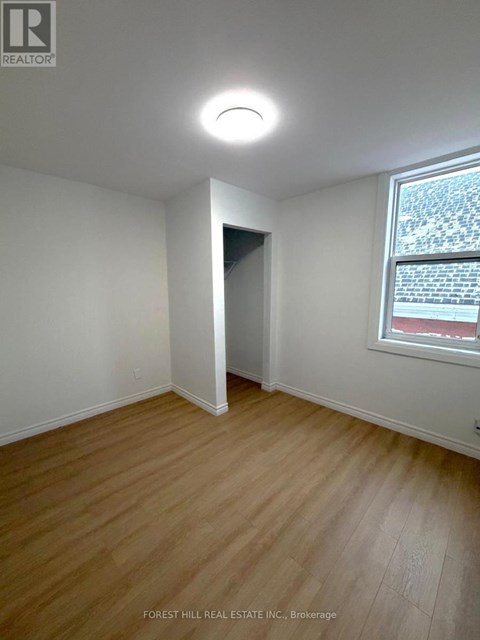 A room with a wooden floor and a window showing a red building outside.