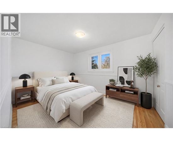 A bedroom with a large bed, a nightstand with a lamp, and a small tree.
