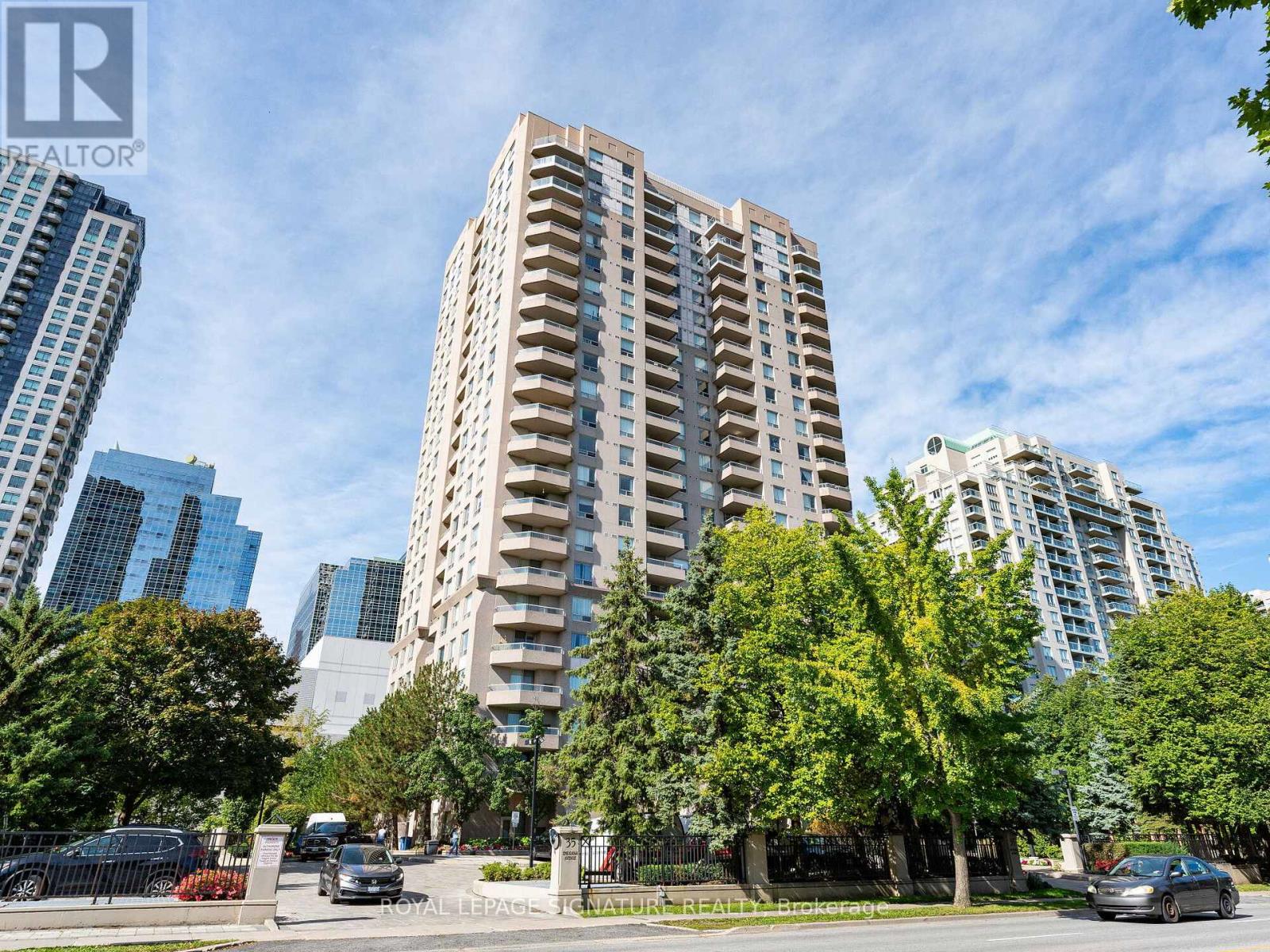 A tall residential building is surrounded by trees and other buildings.