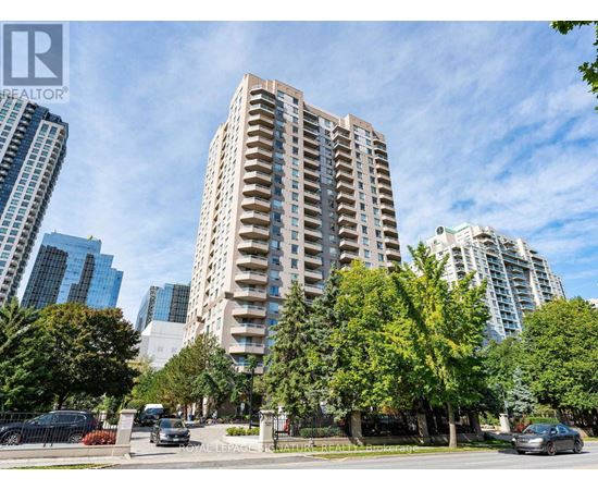 A tall residential building is surrounded by trees and other buildings.