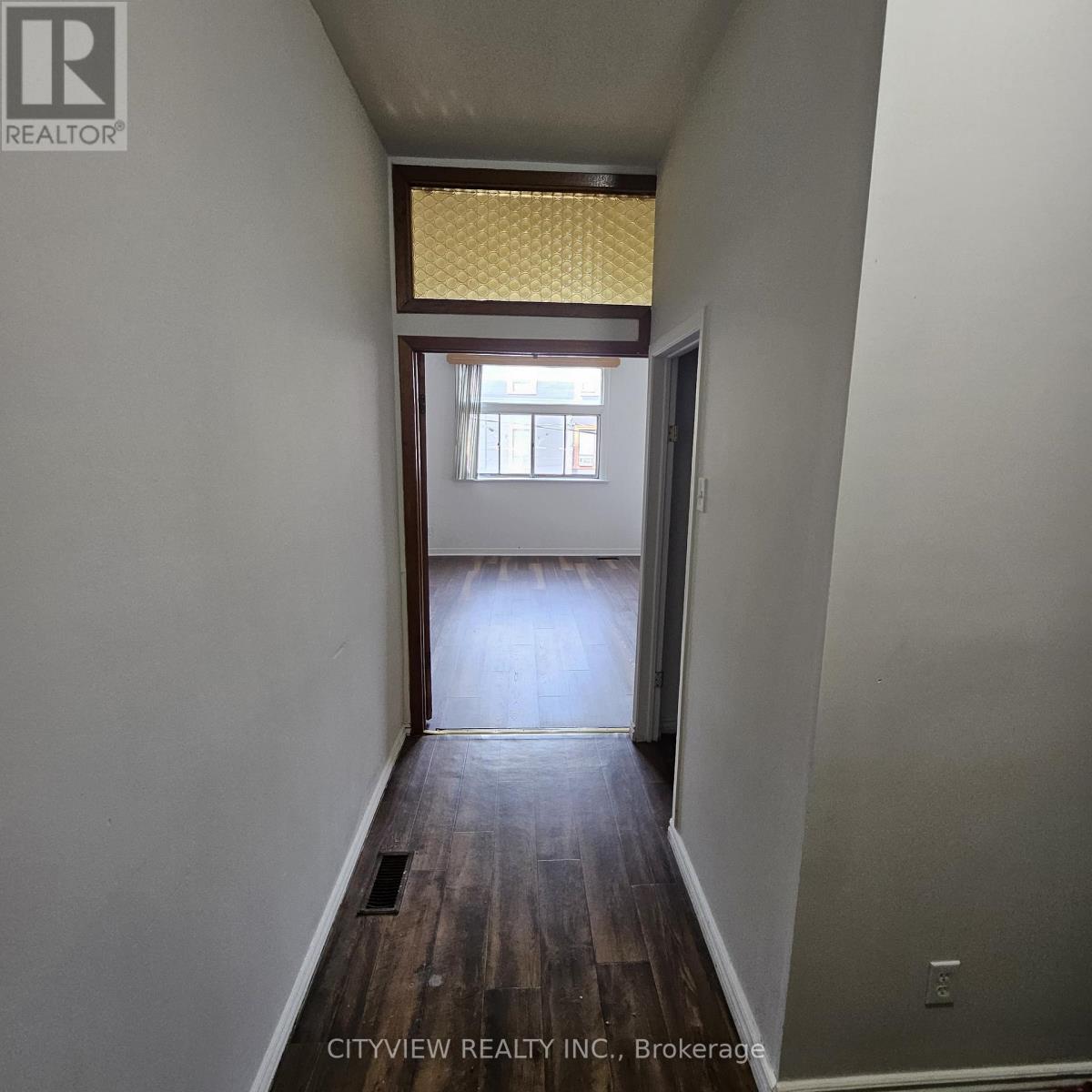 A hallway with wood floors and a window with yellow blinds.