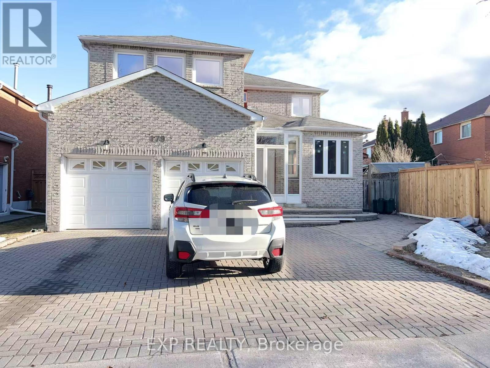 A white car is parked in front of a house with a sign that says EXP Beauty Brokerage.