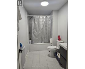 A white washing machine is in a small space with a blue bottle and a red bottle on the floor.