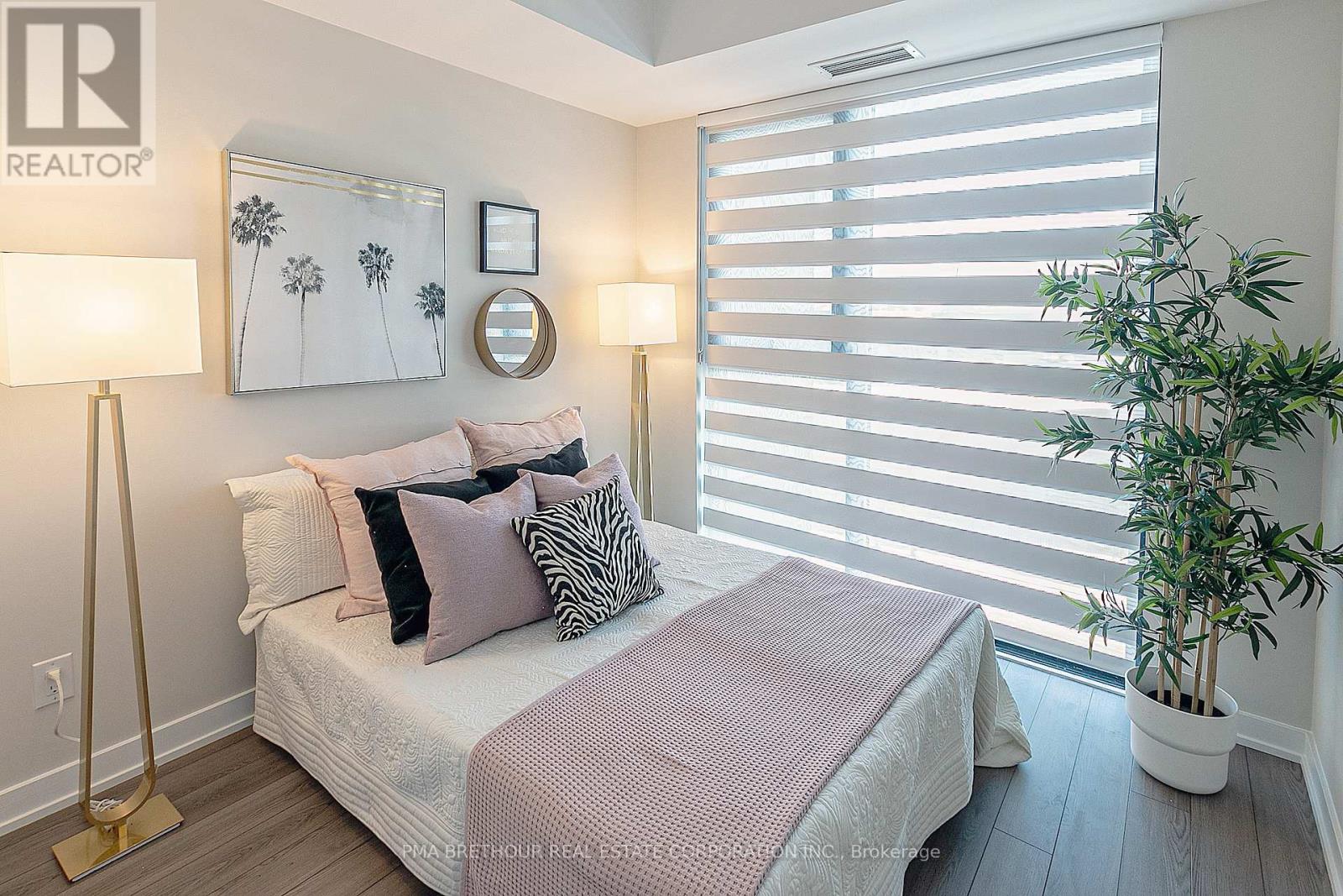 A bedroom with a bed, two lamps, a mirror, and a potted plant.