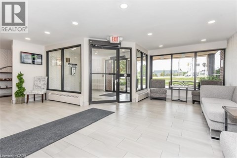 A well-lit, modern living room with a grey sofa and a glass door leading to a balcony.
