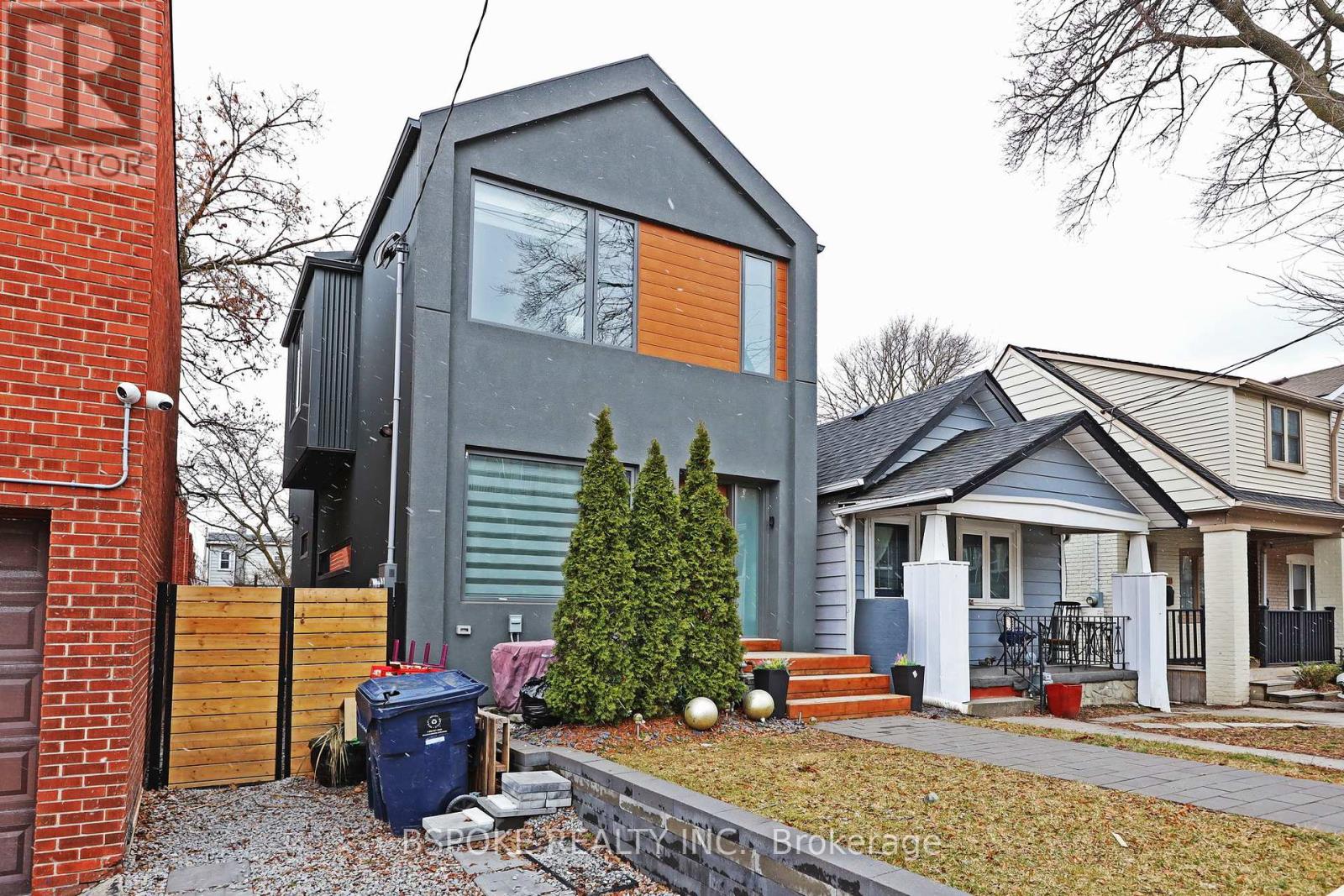 A modern house with a grey exterior and a small tree in front.