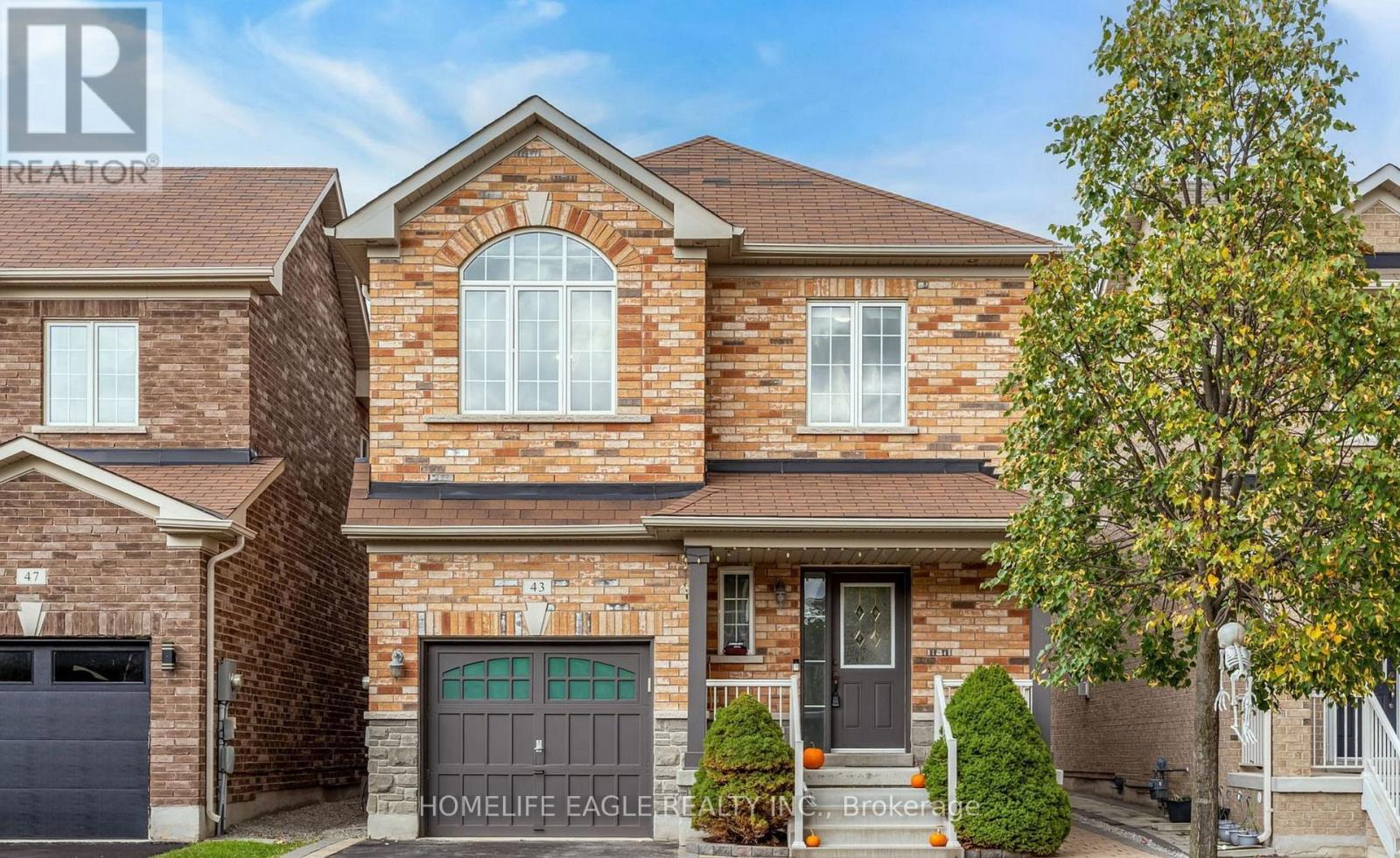 A brick house with a black door and a tree in front.