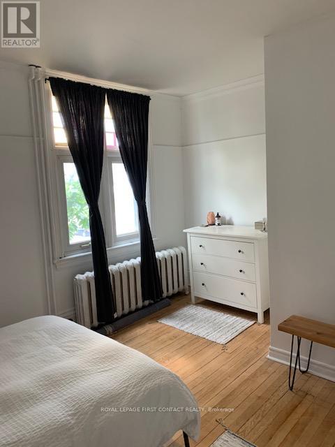 A white bedroom with a window, a radiator, a white dresser, and a wooden bench.