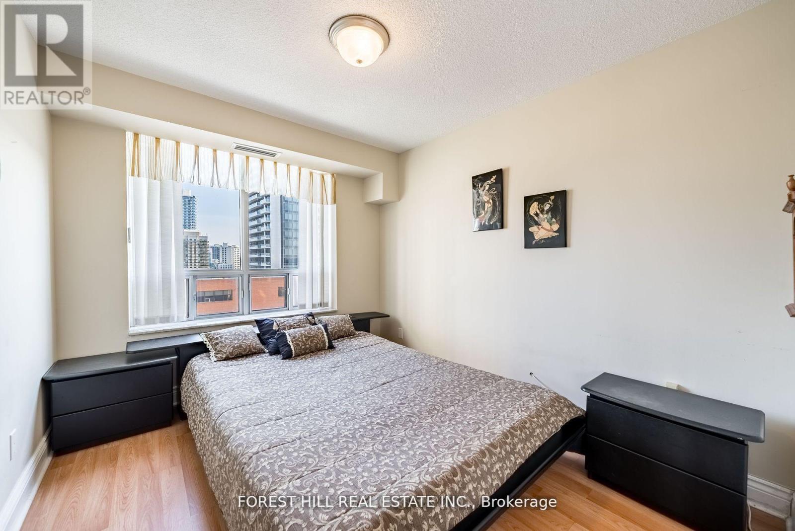 A bedroom with a large bed and a city view through the window.