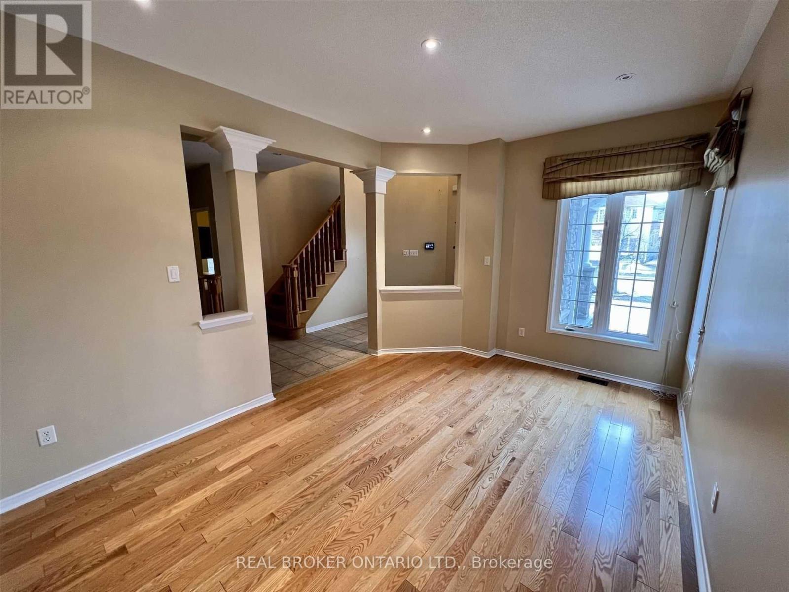 A spacious room with wooden flooring and a staircase leading to another level.