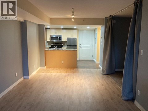 A room with a wooden floor and a kitchenette in the background.
