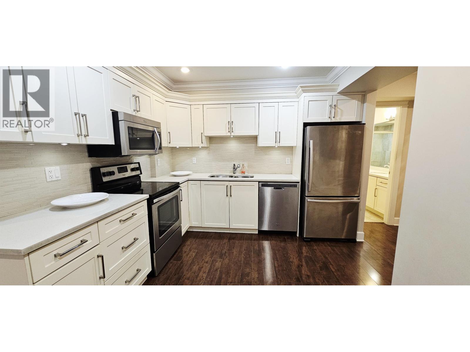A clean, white kitchen with a refrigerator, microwave, oven, and dishwasher.
