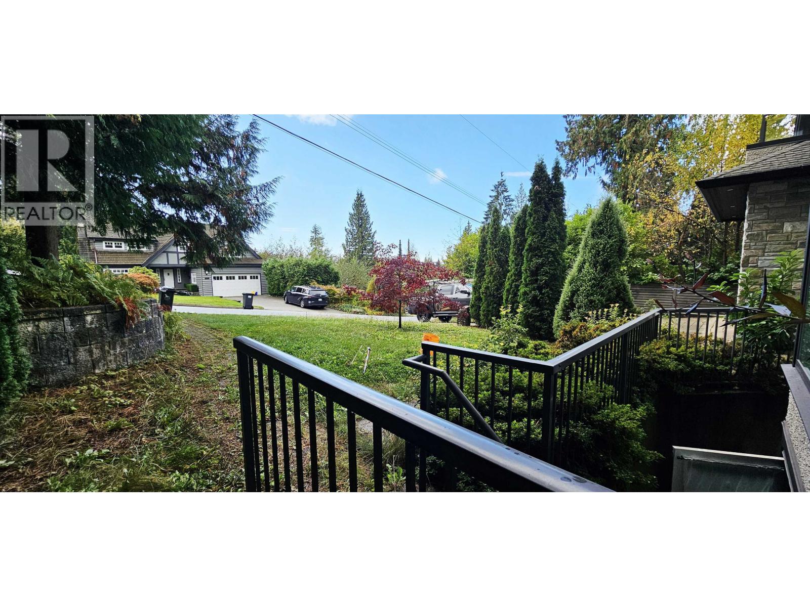 A view from a balcony overlooking a green lawn and trees.