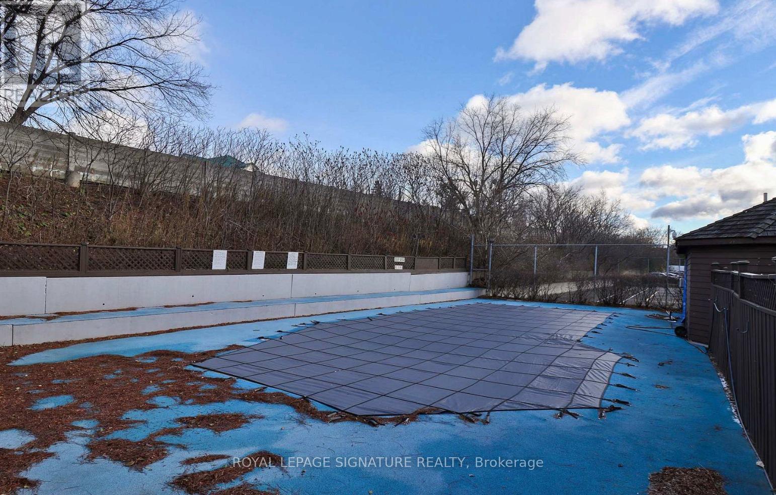 A blue tiled pool area with a fence and trees in the background.