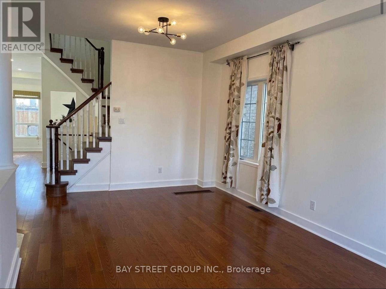 A spacious room with a staircase and a window with curtains.