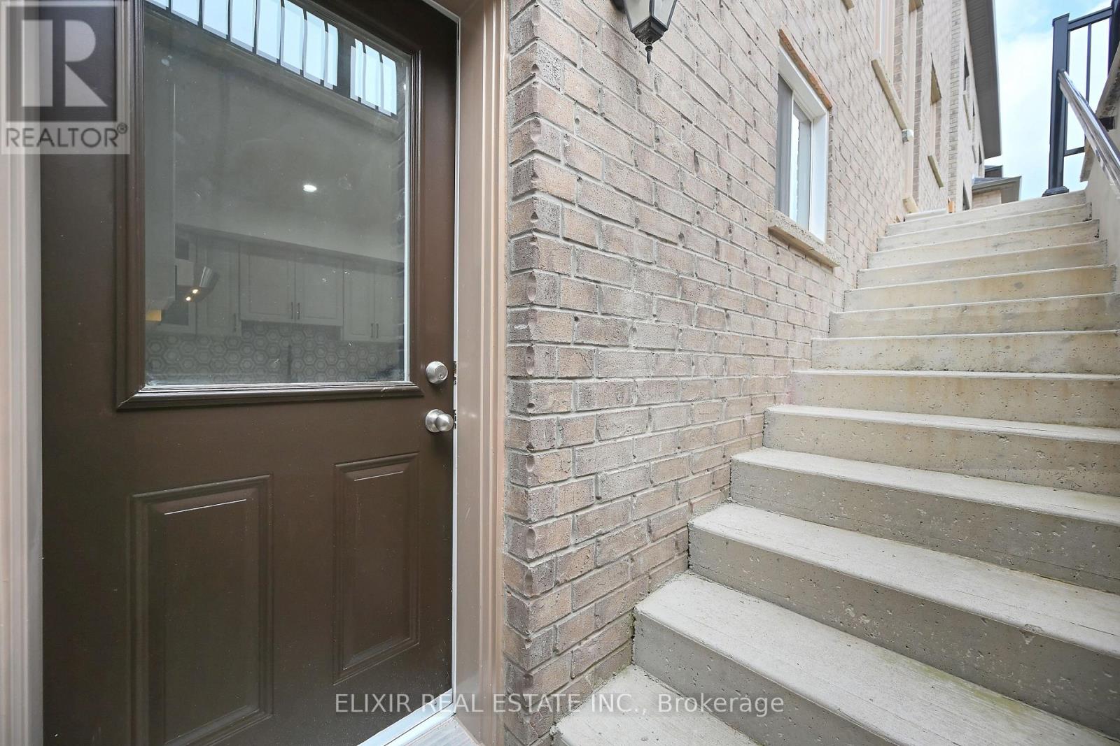 A brown door with a glass window above it and a brick wall to the right.