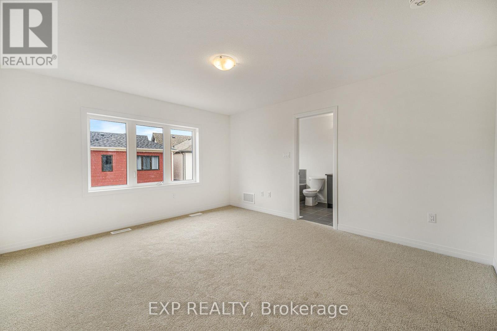 A room with a carpeted floor and a window showing a red building outside.