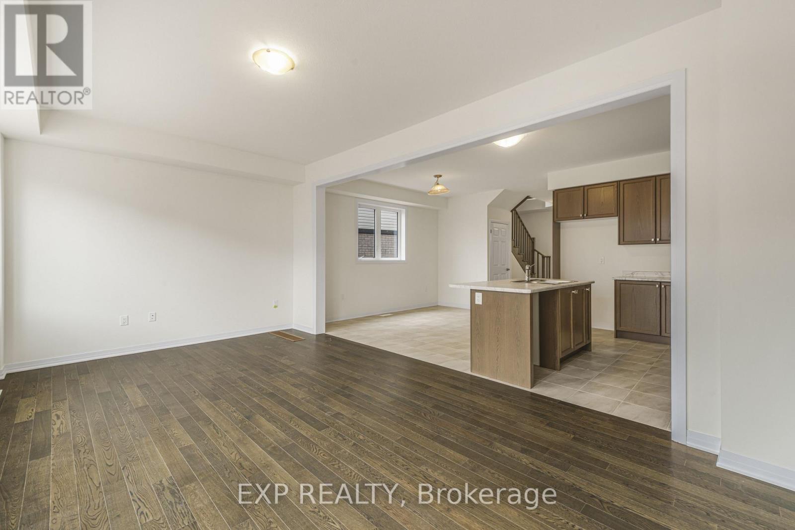 A spacious room with wooden flooring and a staircase in the background.