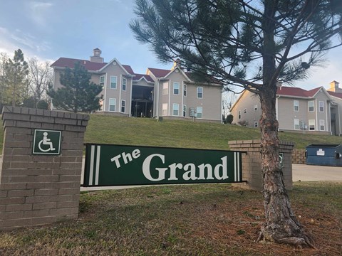 The Grand sign in front of a building with a tree.