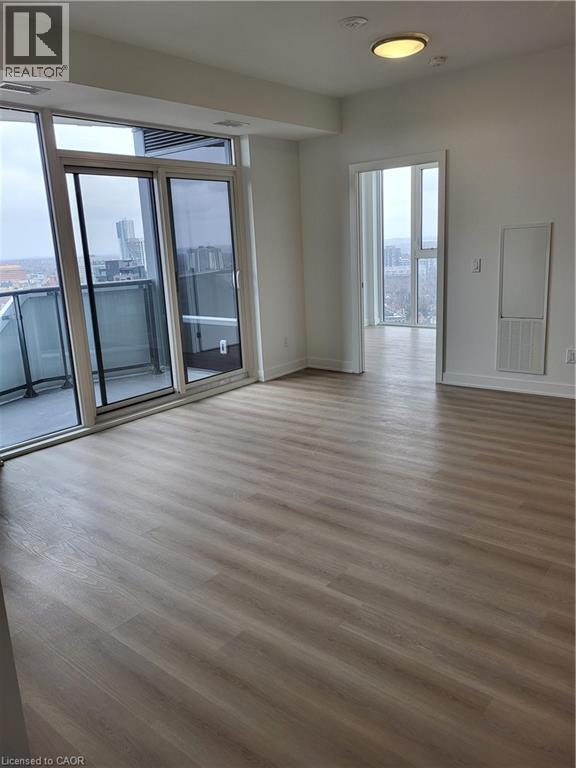 A spacious room with wooden flooring and large windows overlooking the city.