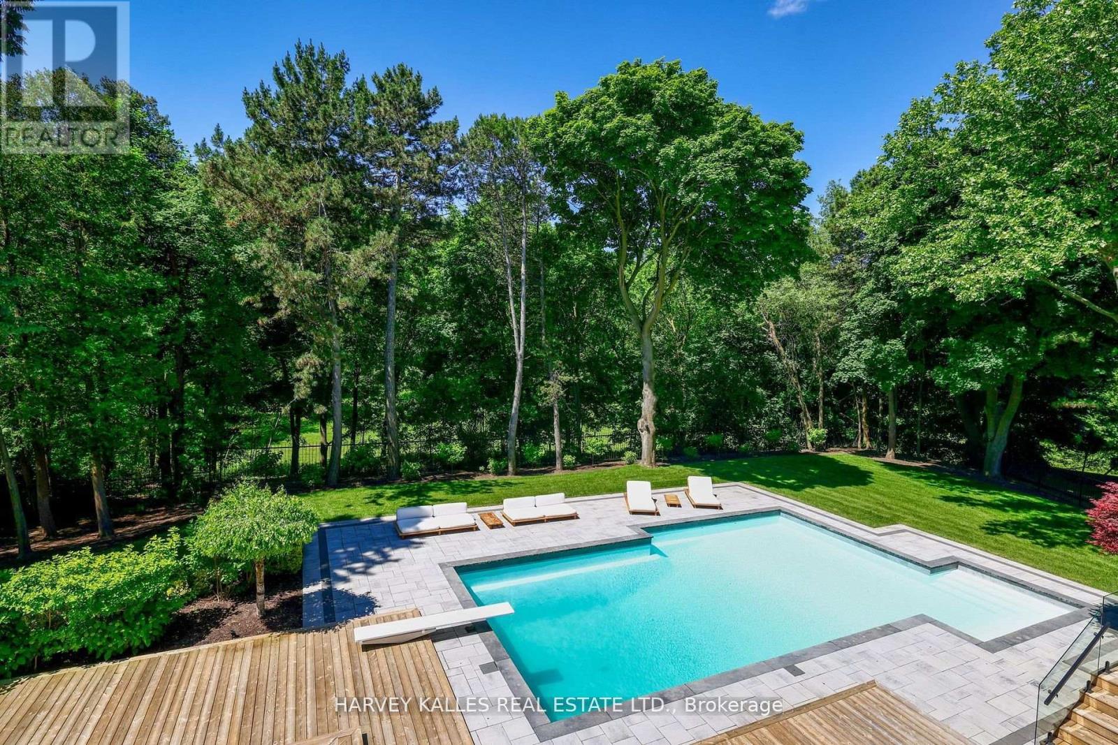 A pool surrounded by trees and a deck with lounge chairs.