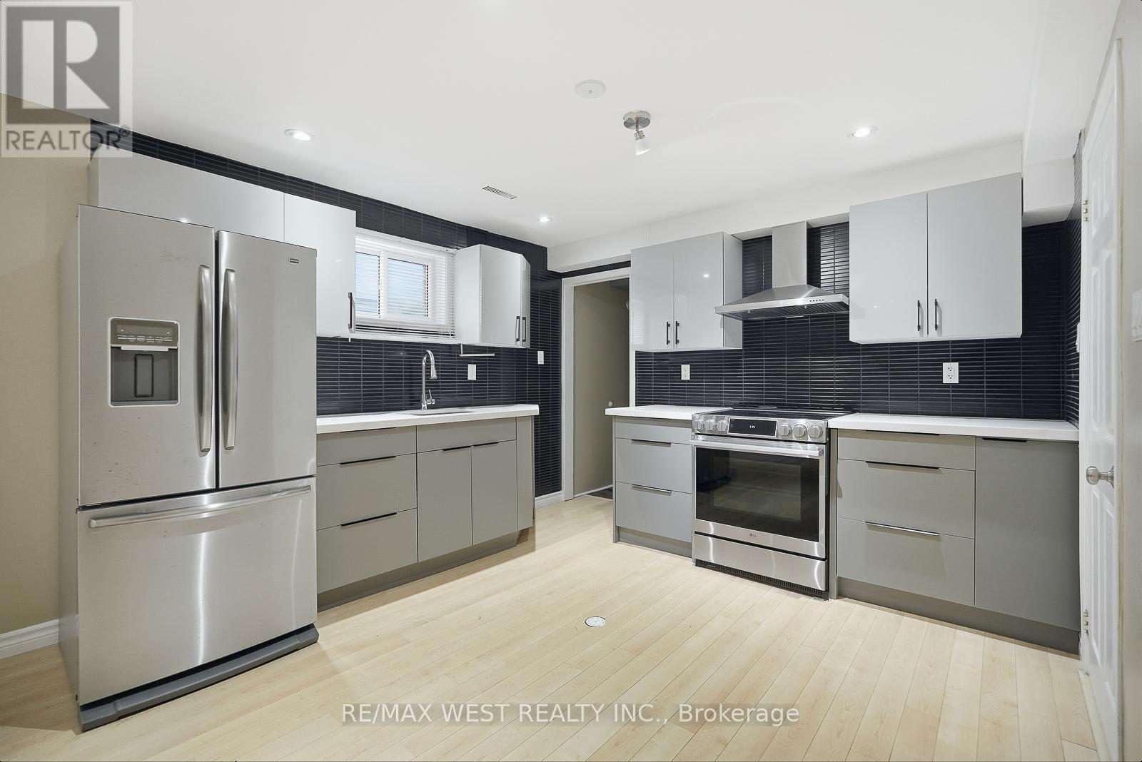 A modern kitchen with a stainless steel refrigerator and wooden flooring.