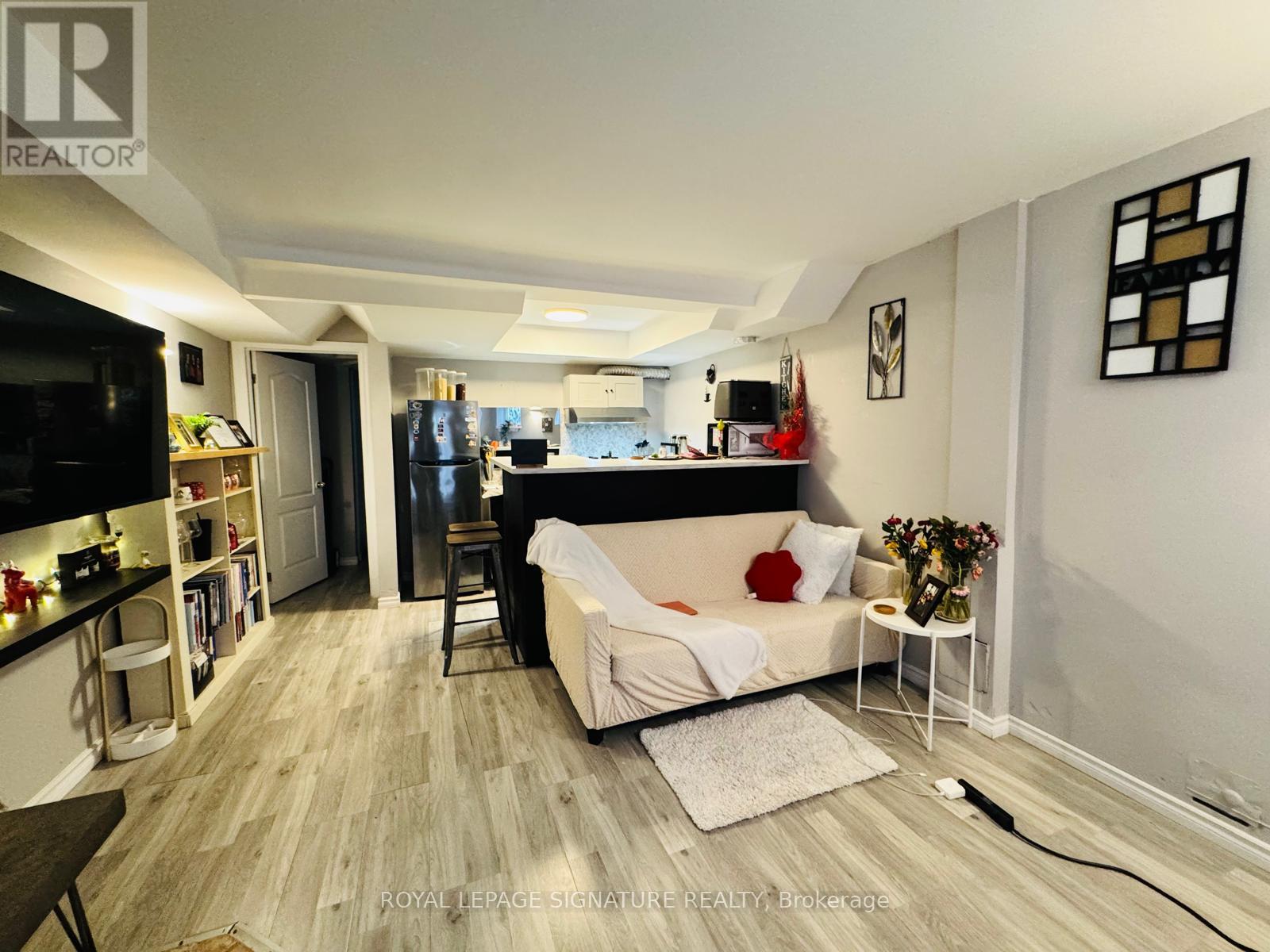 A living room with a couch, a television, and a kitchen area in the background.